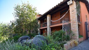 Un bâtiment à deux étages doté d’un balcon, entouré d’une végétation luxuriante et de gros rochers.