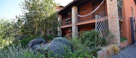 A two-story building with a balcony, surrounded by lush greenery and large rocks.