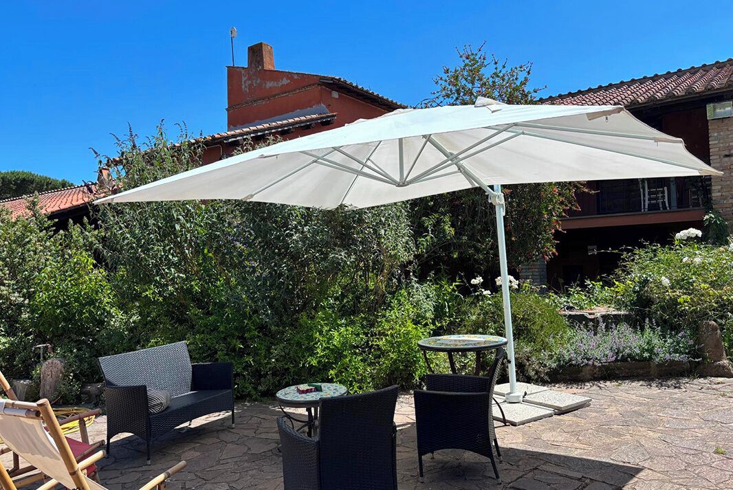 An outdoor patio with a white umbrella, wicker furniture, and a stone floor.