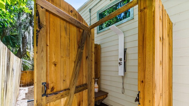 A wooden door leading to a bathroom with a window and a showerhead. - The ArtHouse: Where Industrial Charm Meets Creative Inspiration (St. Augustine)