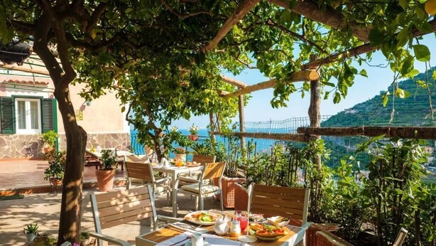 An outdoor patio with wooden furniture, a table set with plates, and potted plants. - Villa Carlotta Minori (Minori)