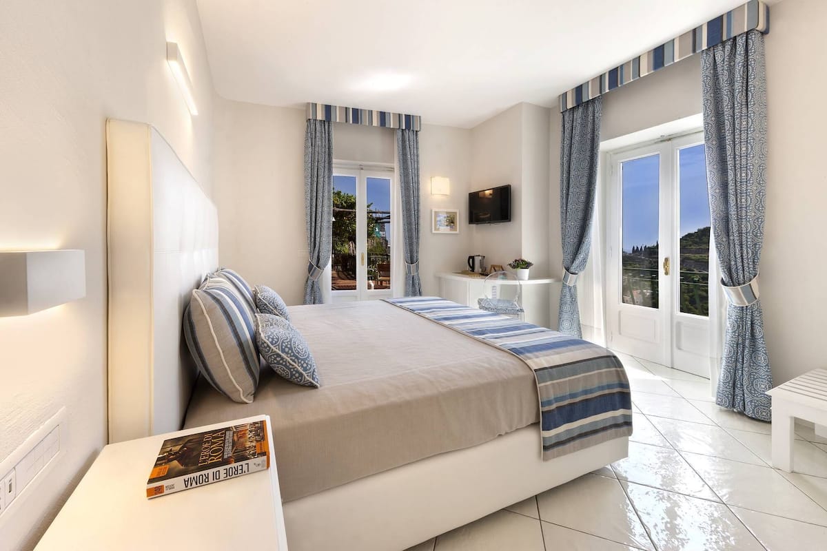 A bedroom with a bed, bedside tables, a TV, and a view of the outdoors.