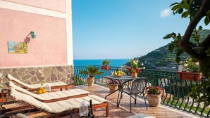 A balcony with lounge chairs, a table with fruit, and potted plants. - Villa Carlotta Minori (Minori)