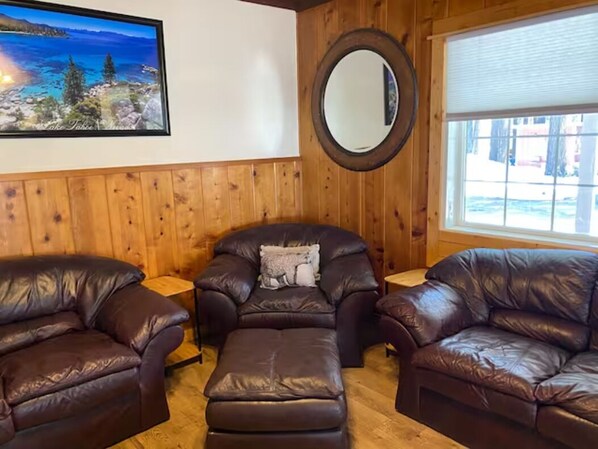A room with wooden paneled walls, a large window, and three leather sofas arranged in a U-shape.