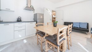 Ett modernt kök med vita skåp, ett kylskåp i rostfritt stål och ett matbord i trä med vadderade stolar.