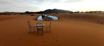 Paisaje desértico con una zona de tiendas blancas y una mesa con sillas al frente.