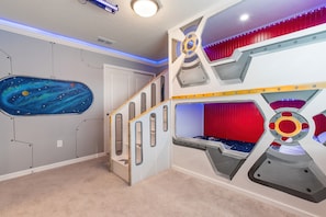 Quarto com beliche, parede com tema de galáxia e cortina vermelha.