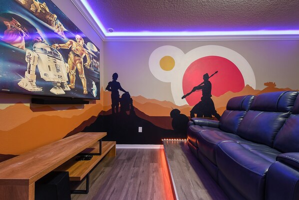 Une pièce décorée d’une fresque murale sur le thème de Star Wars, avec un canapé en cuir et un banc en bois.