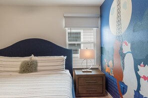 Cozy retreat with a vibrant mural, plush bedding, and a modern lamp.