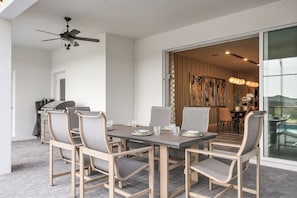 Uma área de refeições ao ar livre com mesa e cadeiras, um ventilador de teto e vista para uma sala de jantar.