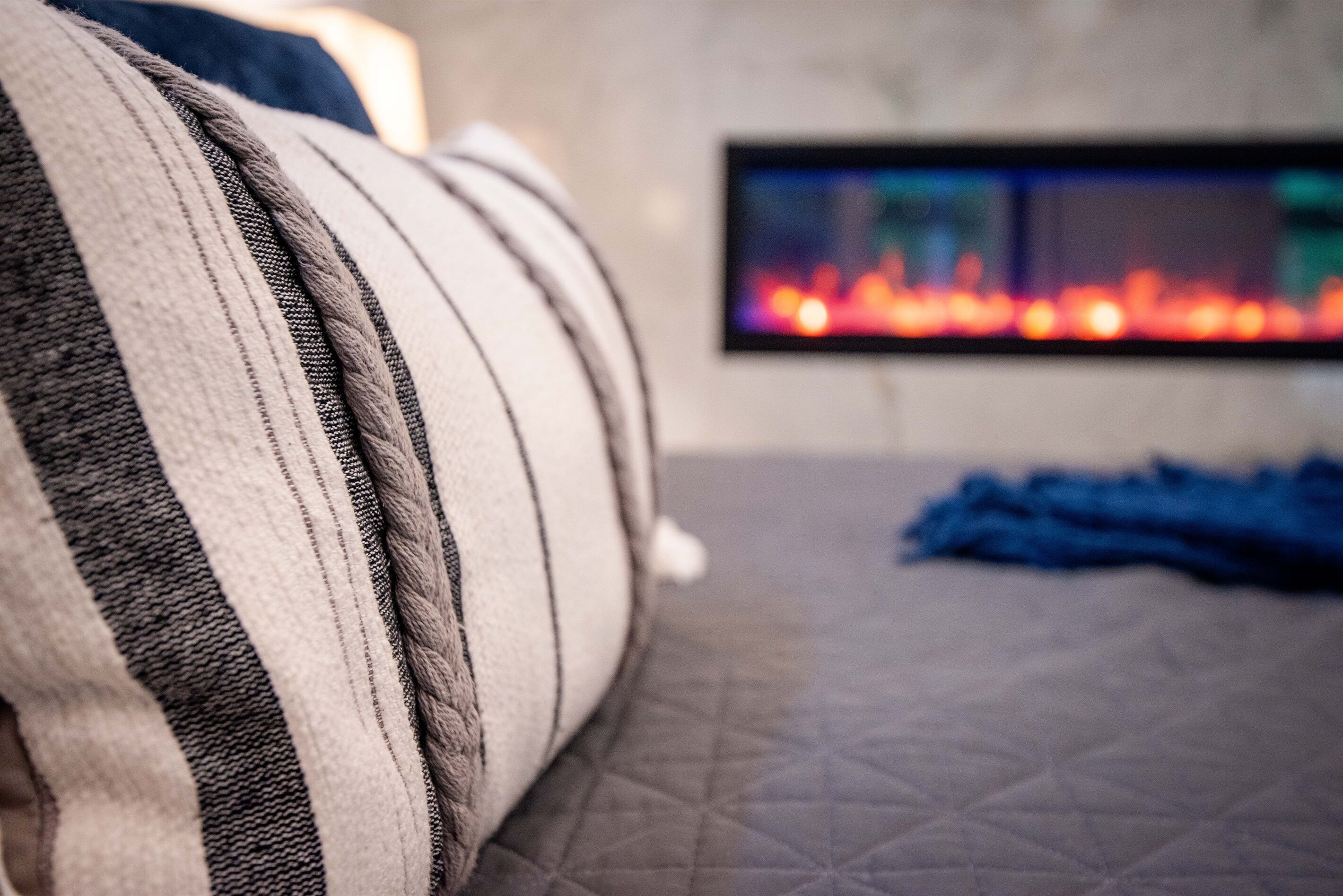 A bed with striped bedding and a quilted mattress, a flat-screen TV mounted on the wall, and a blue blanket on the floor.