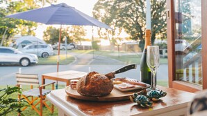 A rustic table with a loaf of bread, a knife, a bottle, and a glass on a wooden board. - Hamptons on Queen - Sunset Water Views (Bongaree)