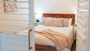 A bedroom with a wooden headboard, a bed with multiple pillows, and a beige blanket. - Hamptons on Queen - Sunset Water Views (Bongaree)