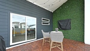 A patio with a brick floor, two wicker chairs, a small table, and a glass door leading to a deck.