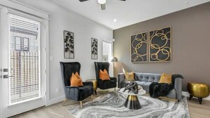 A modern living room with a grey sofa, two black armchairs, a marble rug, and decorative wall art.