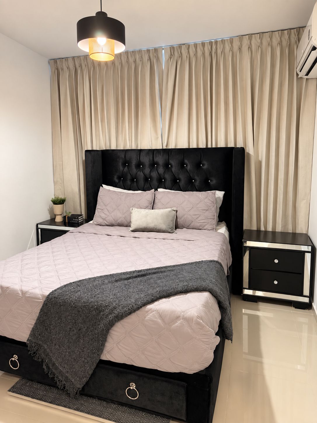 Un dormitorio moderno con un cabecero capitonado, una cama con cubrecama acolchado, dos mesitas de noche con cajones y una lámpara colgante.