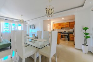 A modern living room with a glass dining table, white chairs, a green sofa, and a chandelier.