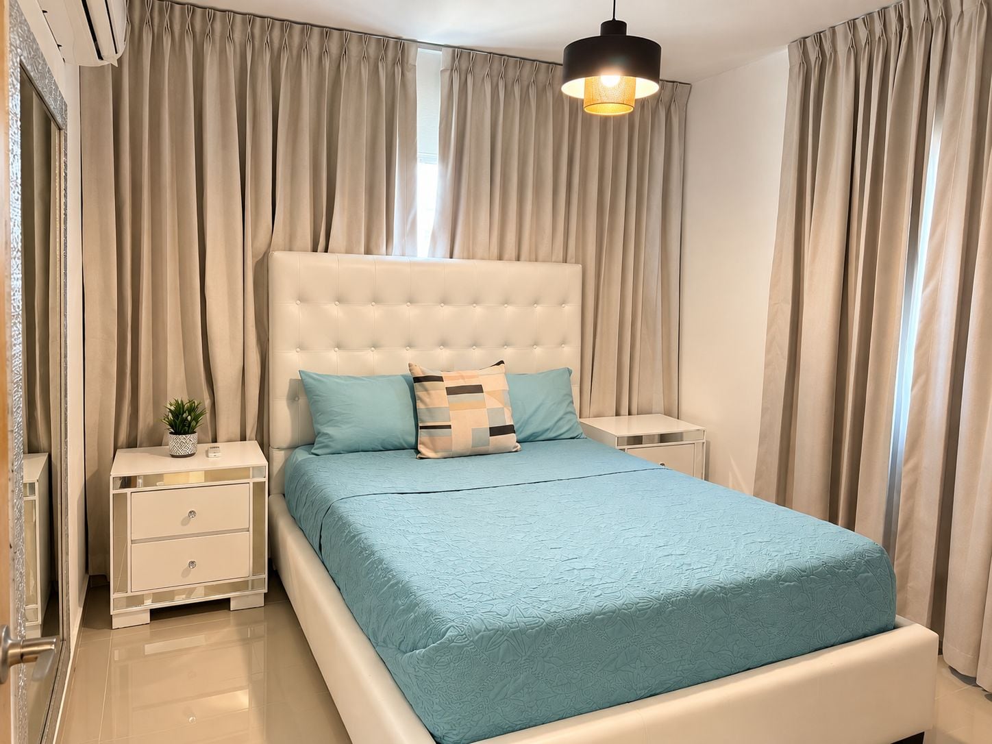A bedroom with a tufted headboard, a bed with a blue bedspread, two bedside tables, and a hanging light fixture.