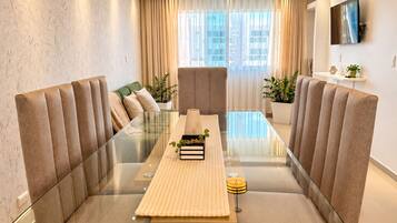 A modern dining area with a glass table, cushioned seating, and a view of the cityscape through large windows.