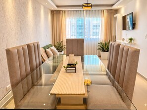 A modern dining area with a glass table, cushioned seating, and a view of the cityscape through large windows.