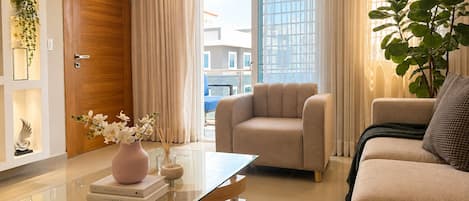 A modern living room with a glass coffee table, beige sofa, and a comfortable armchair.