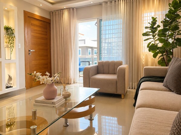 A modern living room with a glass coffee table, beige sofa, and a comfortable armchair.