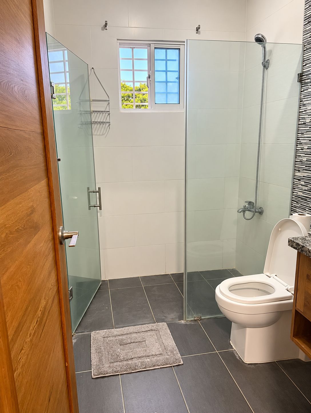 Une salle de bain avec une douche à parois de verre, des toilettes et une petite fenêtre.
