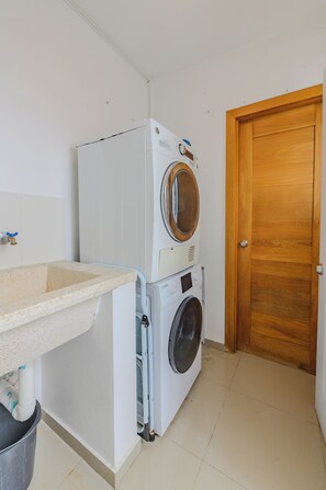 A laundry room with a washing machine and dryer stacked together, a sink, and a wooden door.