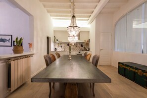 A dining room with a long table, chairs, a chandelier, a radiator, a potted plant, and a large window. - Florence Apartments - Chandelier Apartment (Florence)