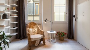 Une pièce comprenant un fauteuil à motifs, une petite table d’appoint, une plante en pot, un lampadaire et une porte blanche.