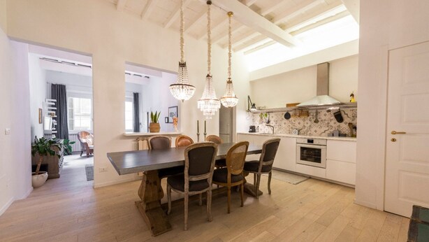 Un coin repas avec une table et des chaises en bois, une cuisine avec des meubles blancs et une porte blanche.