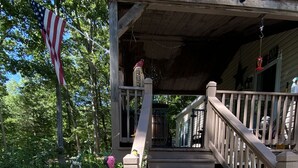 A wooden staircase leading to a covered porch with a bird feeder and a hanging American flag.