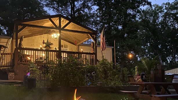 A covered outdoor area with a fire pit, a flag, and a wooden structure with a roof.