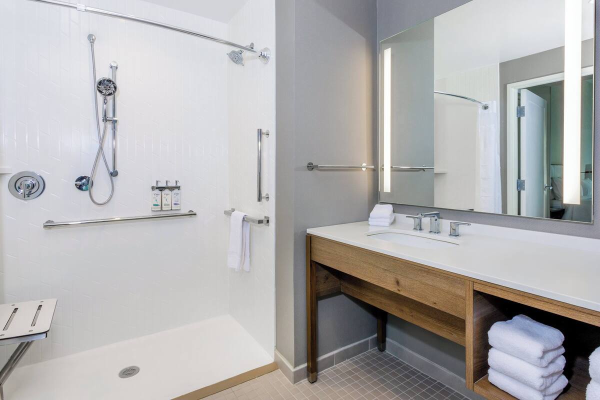 Un baño moderno con ducha, tocador con espejo y barra para toallas.