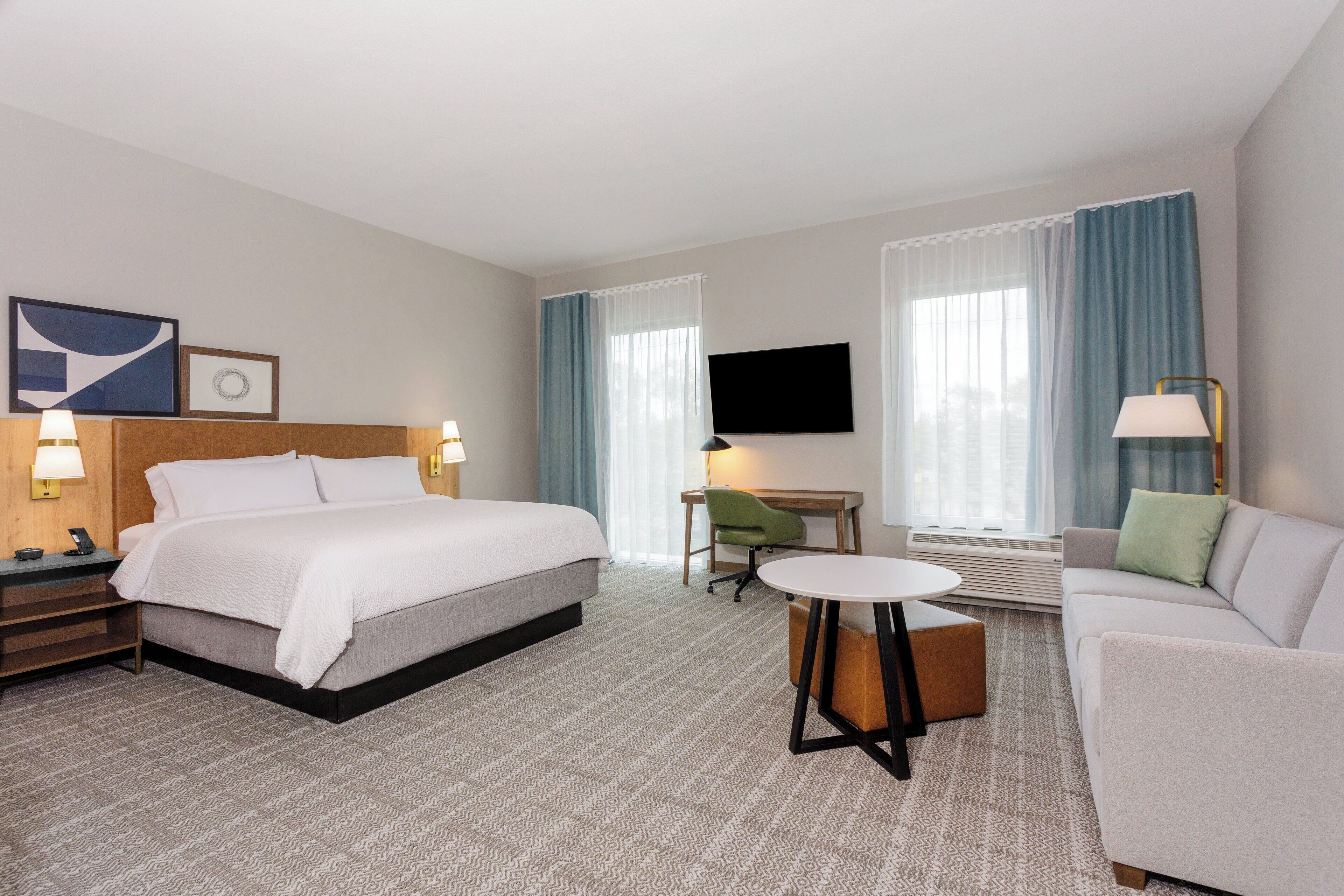 A hotel room with a bed, a desk, a chair, a sofa, and a TV.
