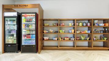 A pantry area with two refrigerators stocked with beverages and snacks, and shelves with various food items.
