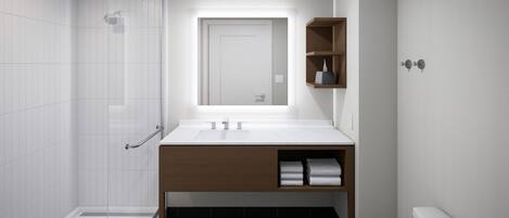 Un baño moderno con cabina de ducha de vidrio, un lavamanos blanco sobre un mueble de madera y un inodoro blanco.