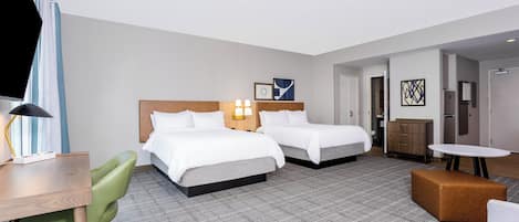 Une chambre d’hôtel avec deux lits, un bureau, une chaise verte, une petite table et un canapé.