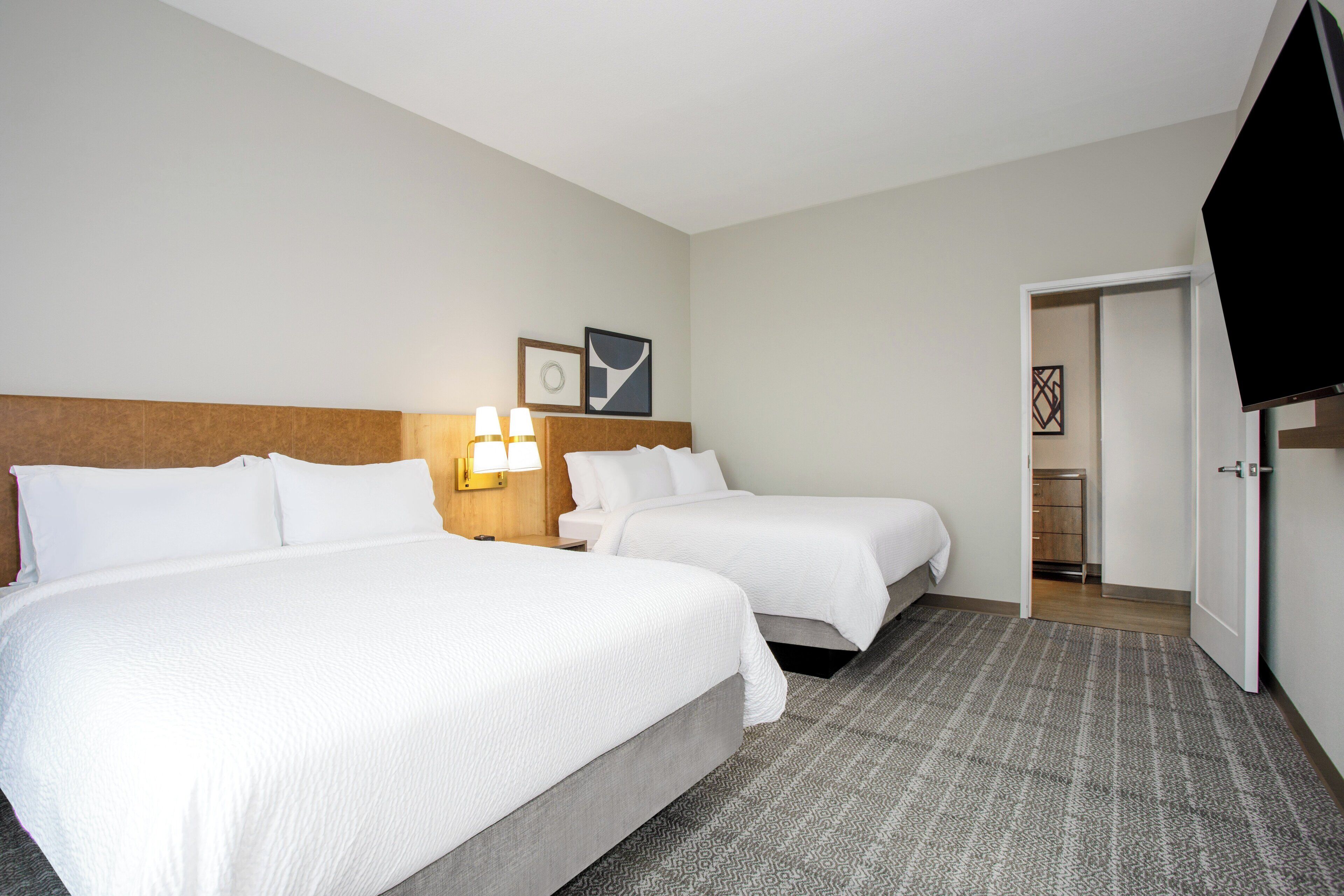A hotel room with two beds, a television, and a door leading to a bathroom.