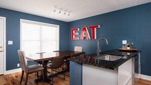 A modern kitchen with a blue wall, a wooden dining table, and a large island with a sink. - EVERYTHING LOUISVILLE GALLERY HOME 15% Discount (Louisville)