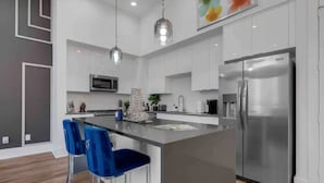 A modern kitchen with white cabinets, a stainless steel refrigerator, and blue bar stools. - Stylish Cozy home near DT Houston and Medical Cntr (Houston)