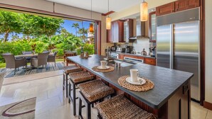 A modern kitchen with a central island, bar stools, and a view of lush greenery.