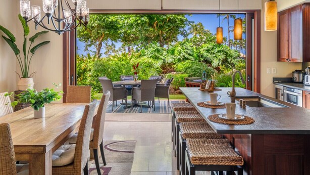 A modern kitchen with a large island, dining area with a view, and a chandelier.