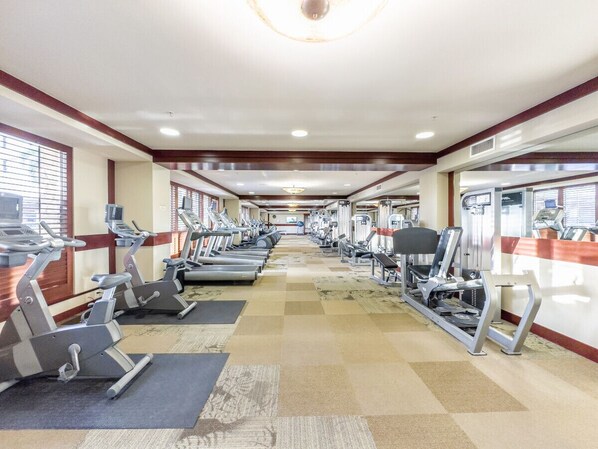 Un gimnasio con cintas de correr, elípticas y equipo de pesas dispuestas en filas.