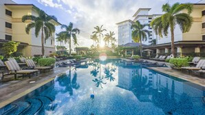A swimming pool with lounge chairs, palm trees, and hotel buildings.