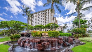 A landscaped garden with a cascading water feature, palm trees, and a building in the background.