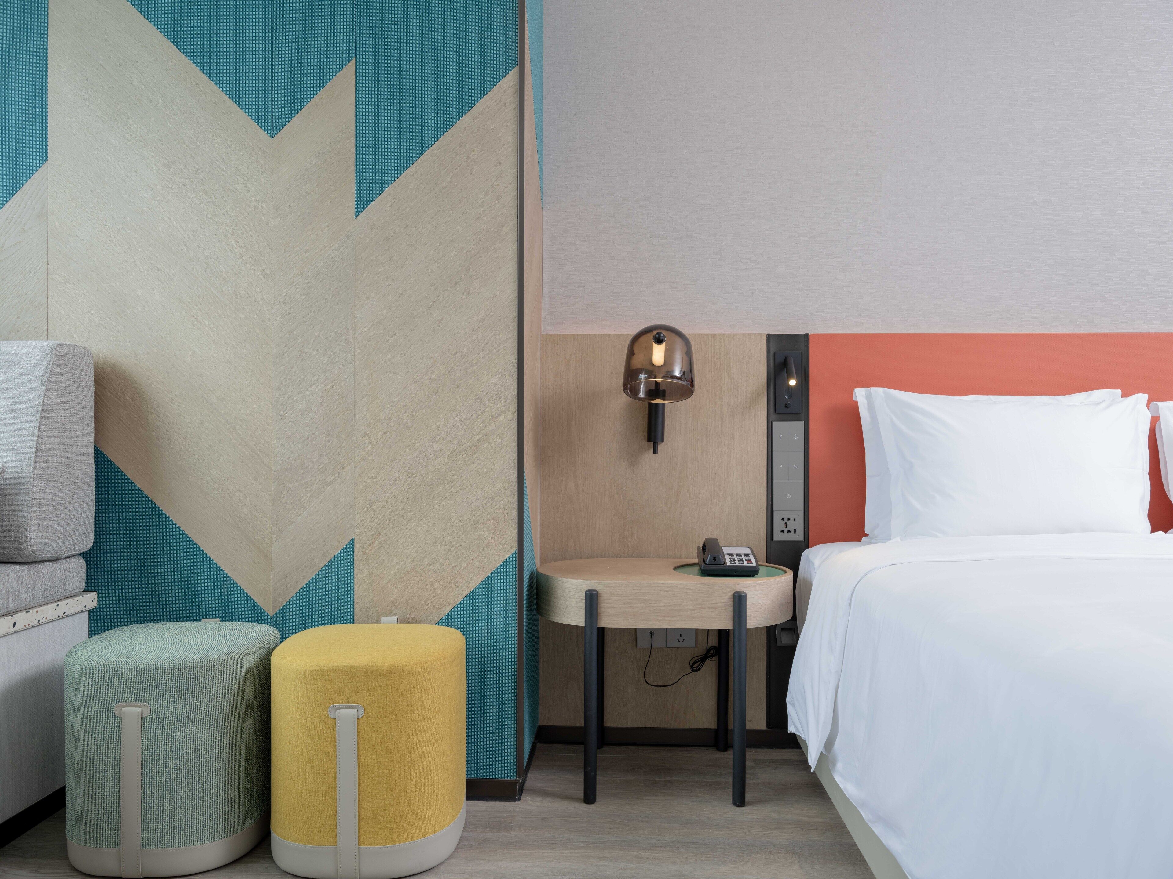 Een hotelkamer met een bed, een bureau met lamp en twee voetenbankjes.