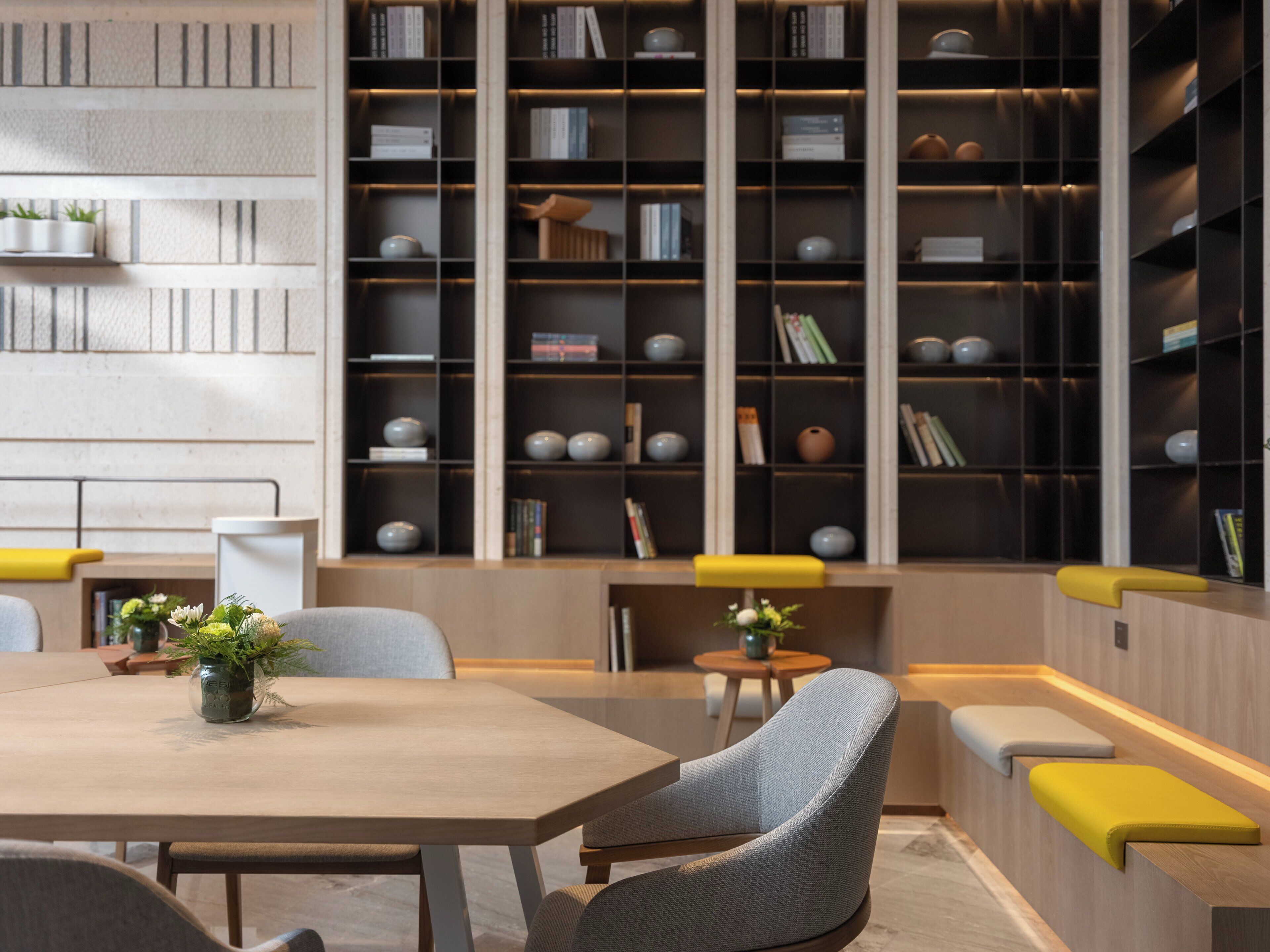 Une bibliothèque moderne, dotée d’étagères, d’espaces de lecture et d’une table agrémentée d’un vase.