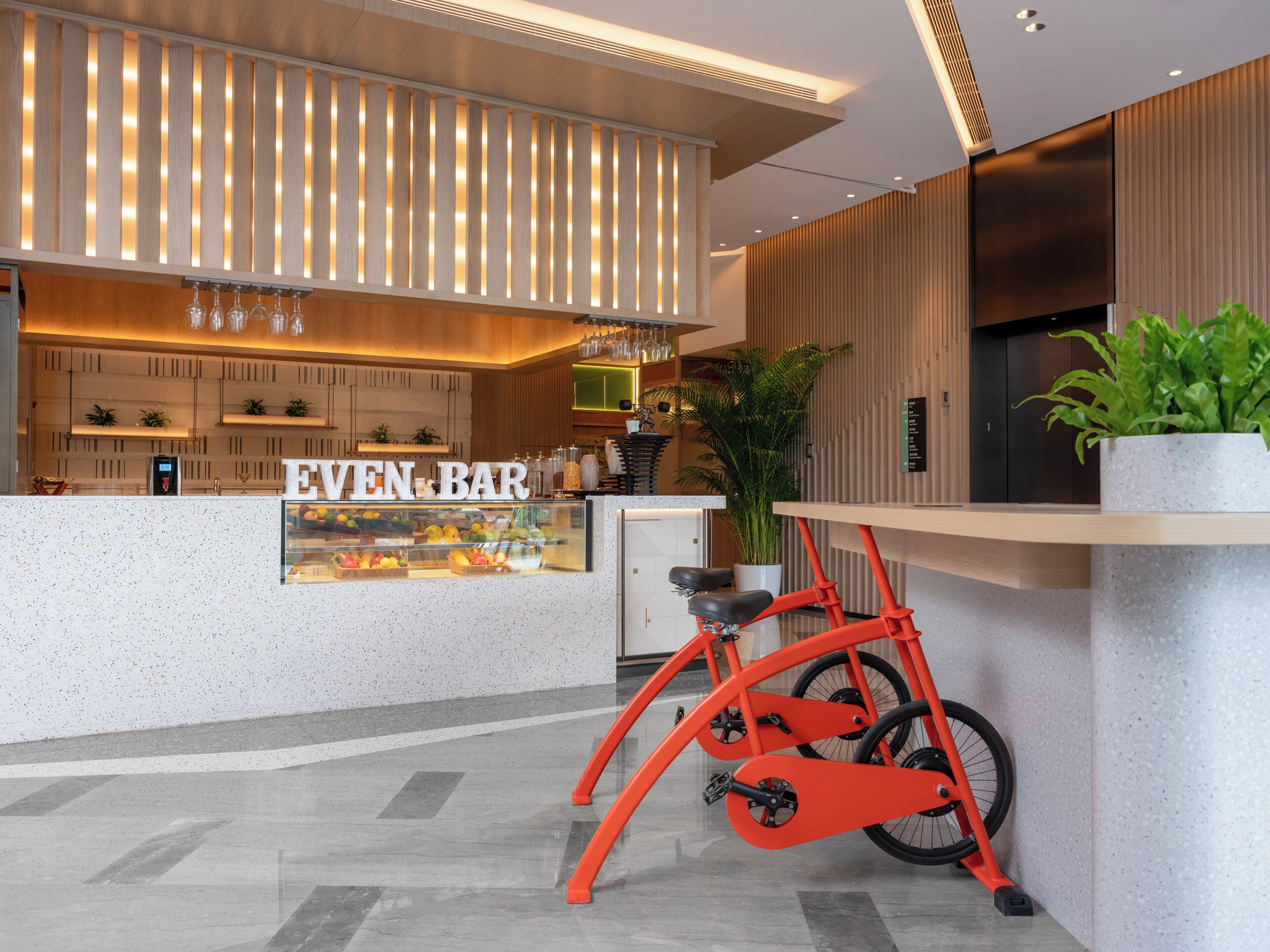 A modern bar area with a glass display case, a bicycle, and a wooden reception desk.