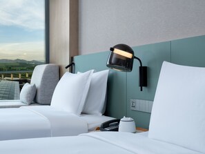 Une chambre d’hôtel avec un lit, une table de chevet, une lampe, un téléphone et une vue sur un pont et des montagnes.